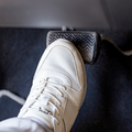 A person wearing white sneakers pressing down on car brake pedals