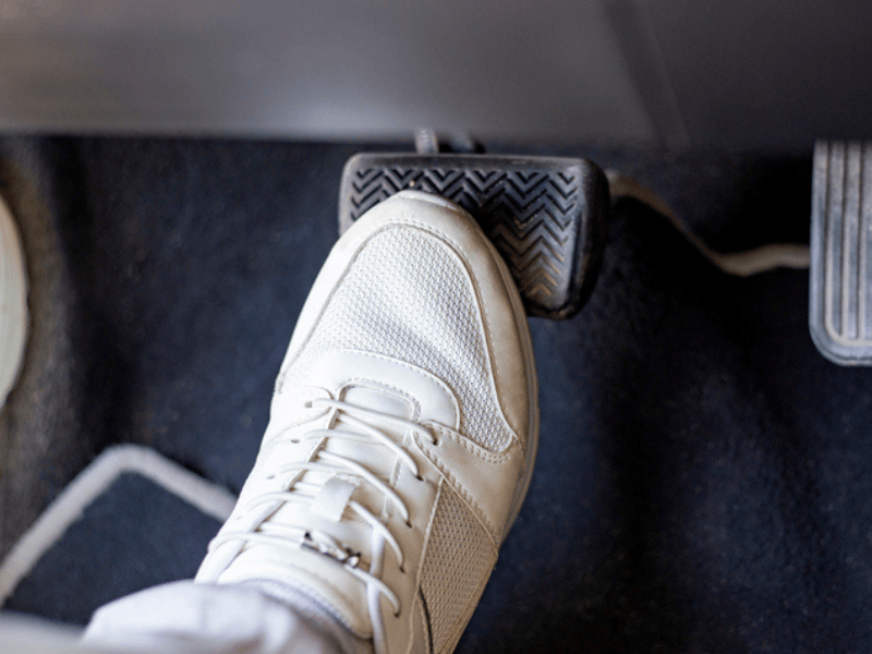 A person wearing white sneakers pressing down on car brake pedals