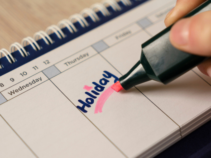 A person writing holiday on a calendar
