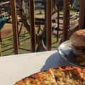 A pizza and burger on a table with a kids play area in the background