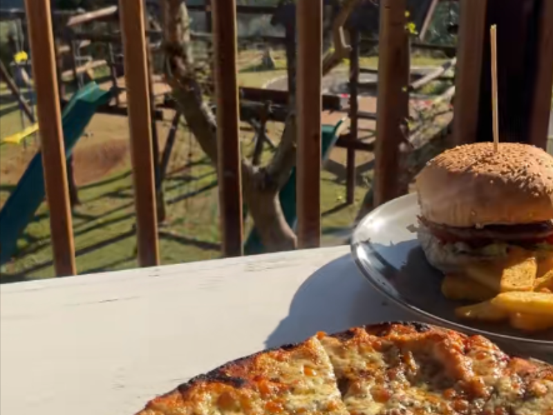 A pizza and burger on a table with a kids play area in the background