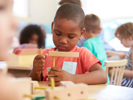 A pupil working at a classroom desk with wooden shapes