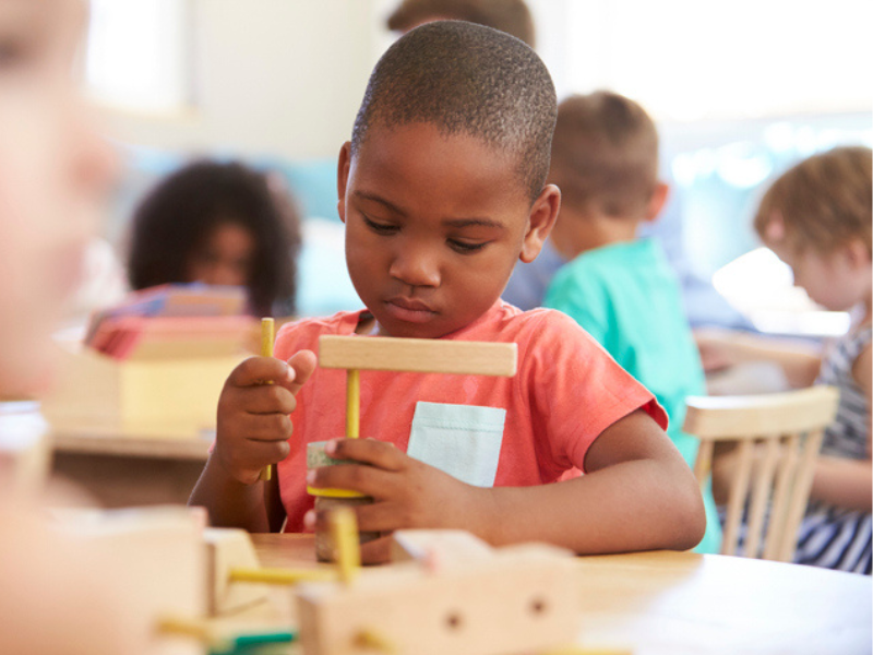 A pupil working at a classroom desk with wooden shapes