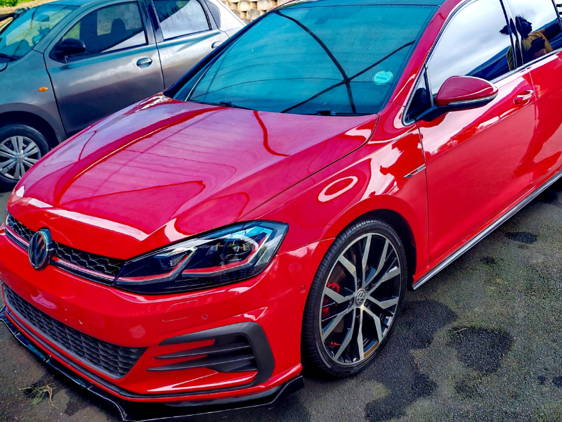 A red Golf GTI parked in a parking spot next to another car