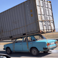 A shipping container tied to the top of a car travelling on the road
