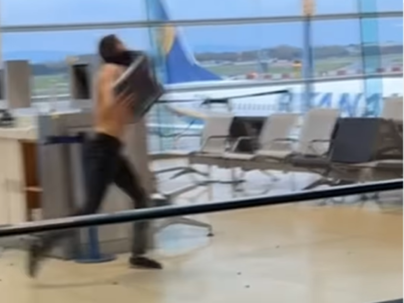 A shirtless man throwing something inside an airport