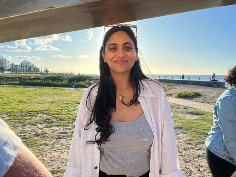 A smiling woman stands close by the beach
