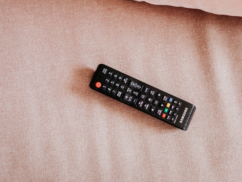 A television remote control lying on pink bed sheet