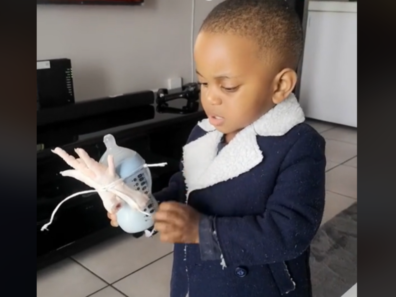 A toddler holding a milk bottle with chicken feet tied to it