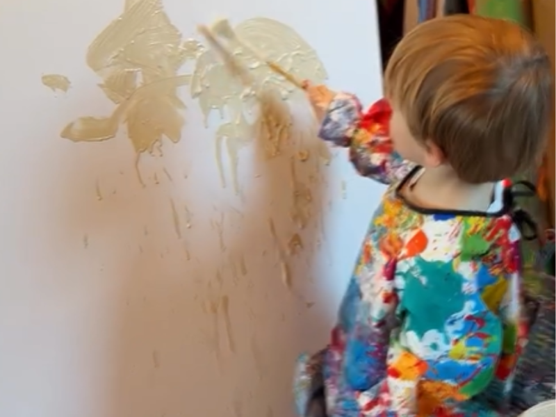 A toddler paints on a large canvas