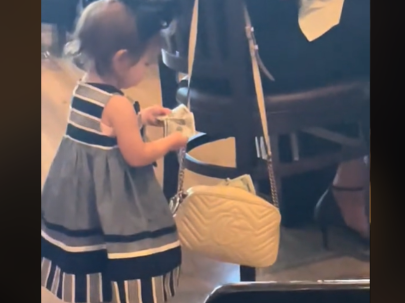 A toddler pulling out money from woman's purse at restaurant