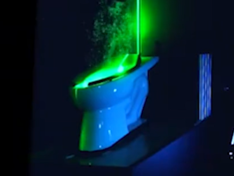 A toilet with a green UV light showing water droplets in the air