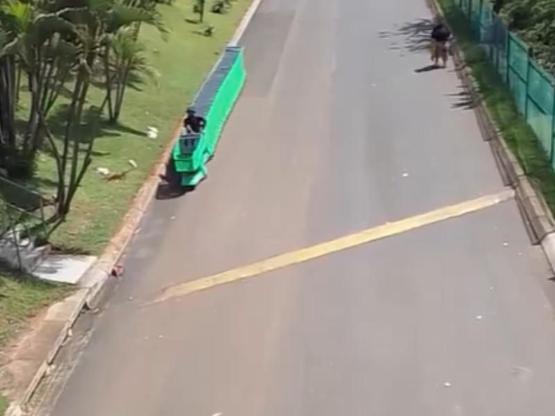 A trolley porter sits on trolleys and rides down a steep hill outside a mall