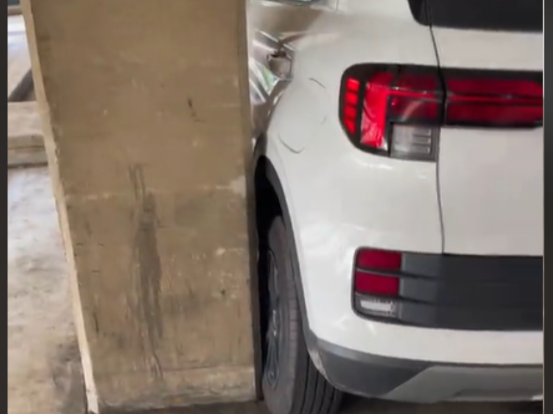 A white car parked close to the pillar inside a parking lot