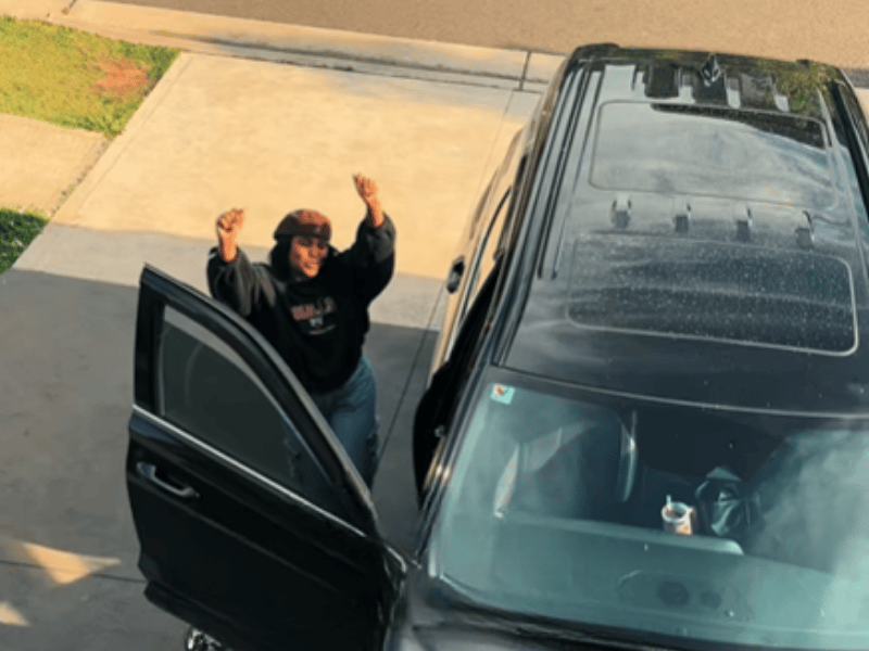 A woman dancing at her car parked in the driveway