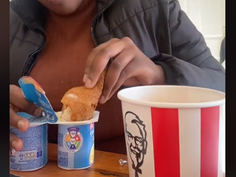 A woman dipping her chicken into a yoghurt container