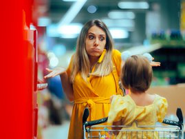 A woman grocery shopping explains frugality to her young daughter