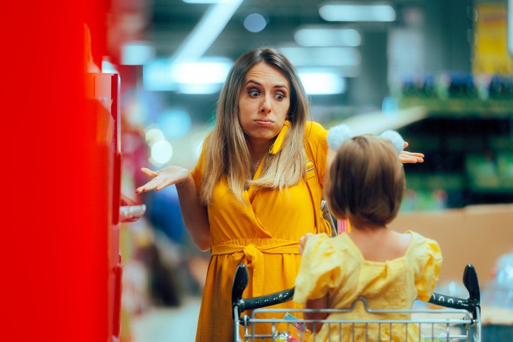 A woman grocery shopping explains frugality to her young daughter