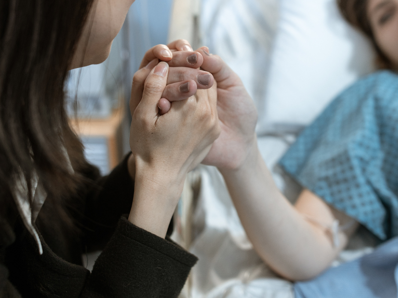 A woman holding a patient's hand in hospital