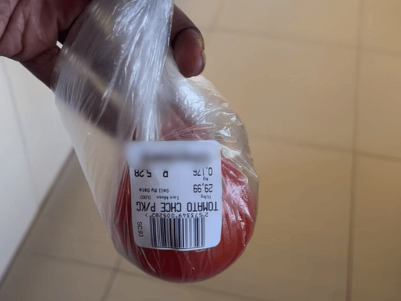 A woman holds up a plastic packet with a tomato inside that has been weighed