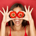 A woman places two tomatoes on her eyes playfully