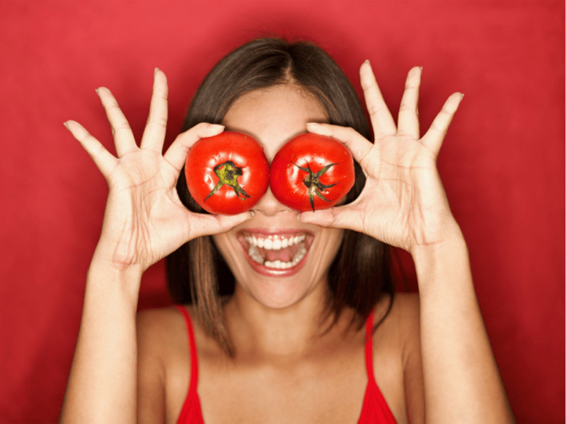 A woman places two tomatoes on her eyes playfully