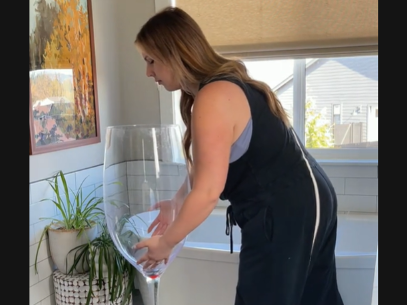 A woman placing a large wine glass on the bathroom floor