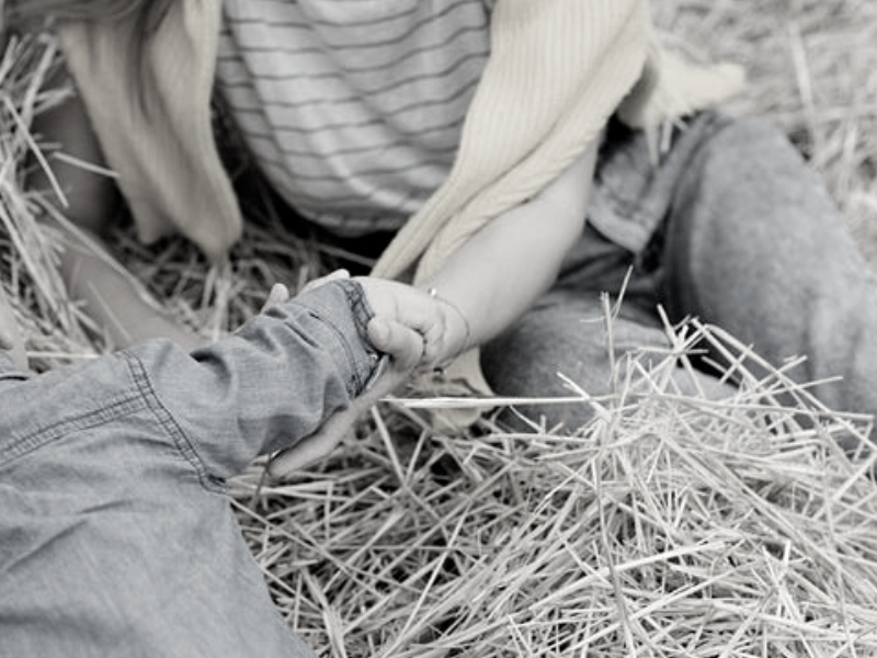 A woman sitting on brown hay holding a boy