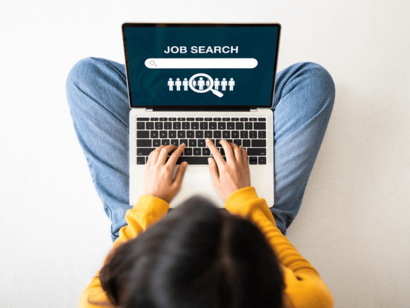 A woman sitting on the floor using her laptop to search for a job