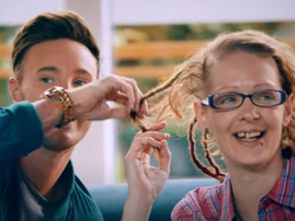 A woman smiles as a man sniffs her badly kept hair