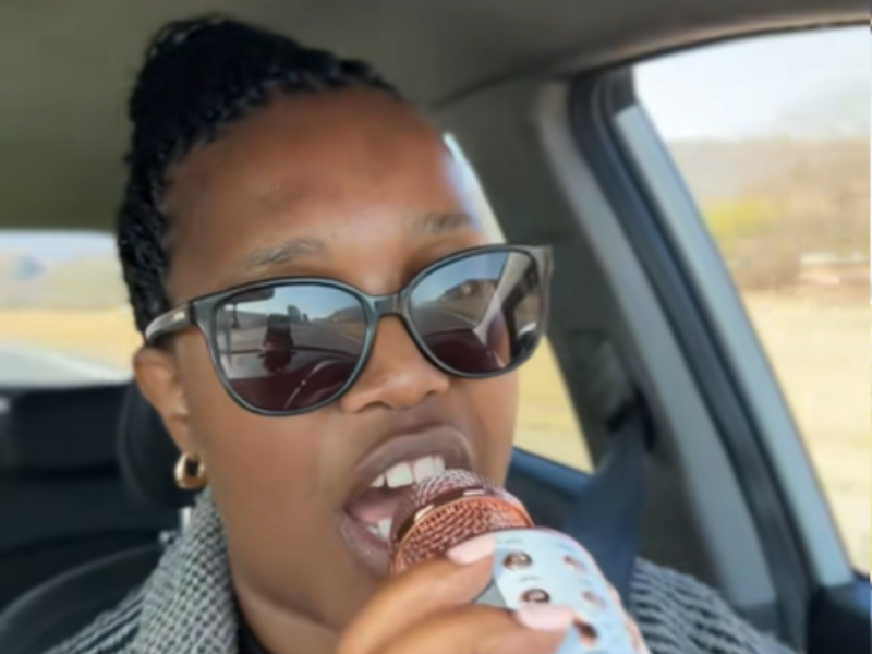 A woman uses a cordless microphone to sing in her car