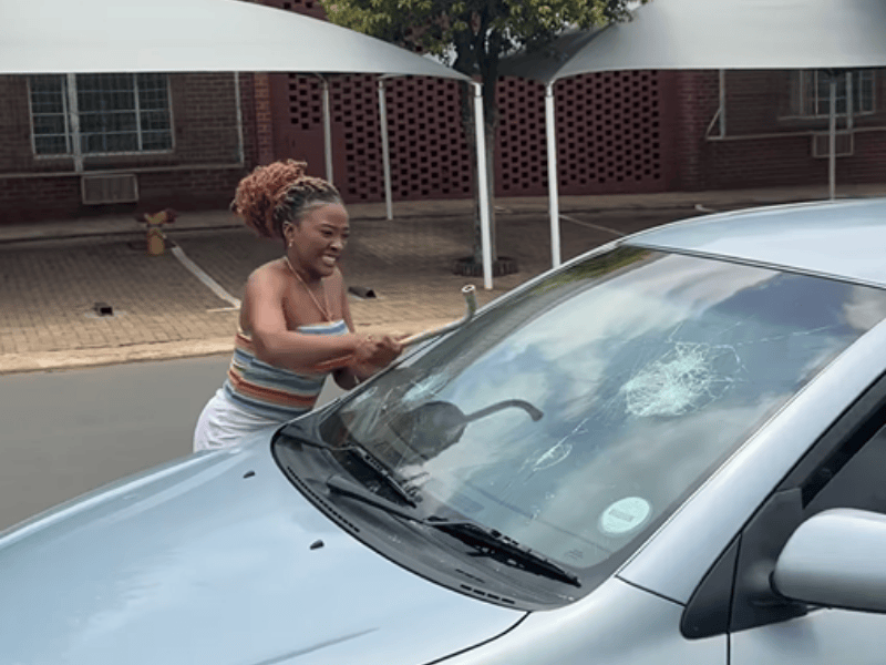 A woman uses a metal object to shatter a car windscreen