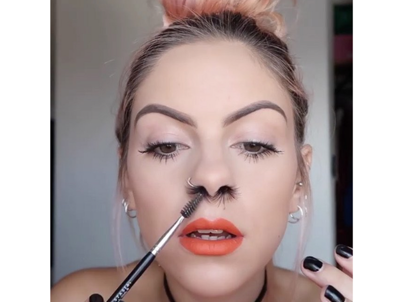 A woman using mascara stick to push in her nose hair extensions