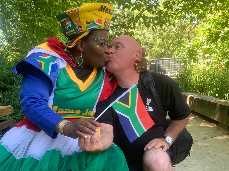 A woman wearing a South African flag-inspired dress kissing a Frenchman