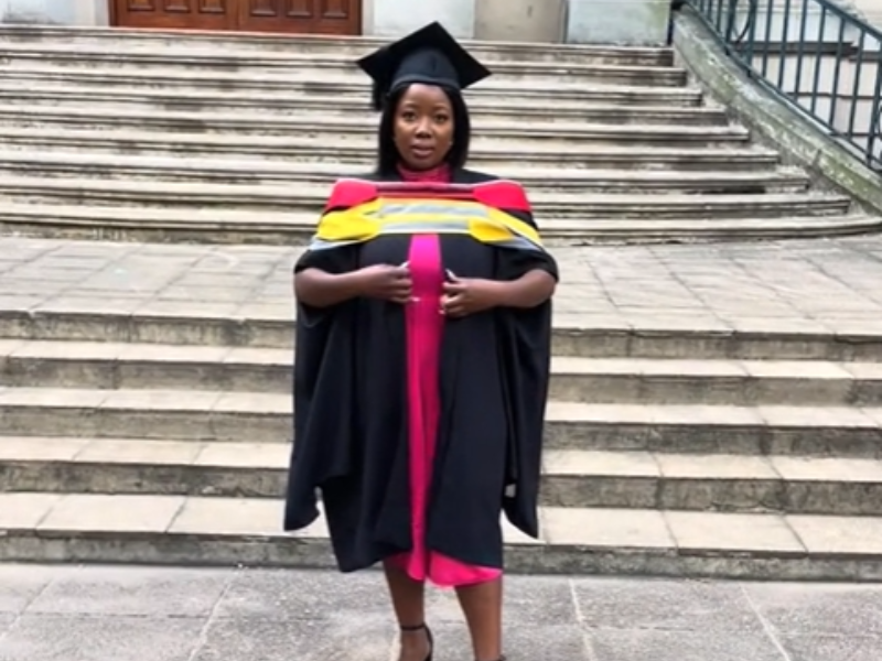 A woman wearing a graduation gown and cap in front of a building
