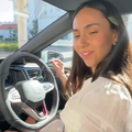 A woman wearing a white dress dances while sitting in the drivers seat