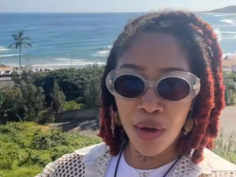 A woman with dreads standing at a resort in KZN with the beach as her background