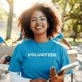 A woman with natural curly hair stands outdoors in front of a volunteer table