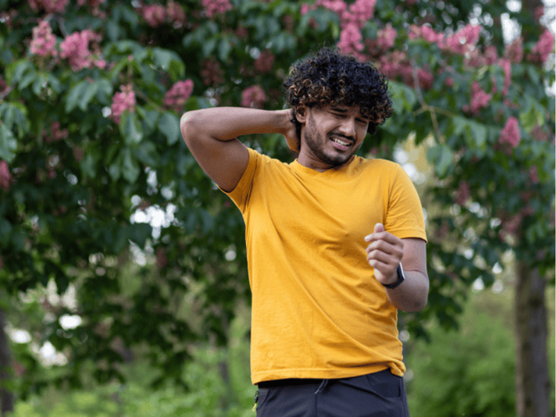 A young Indian man walk in the park and starts itching as he gets bitten by insect