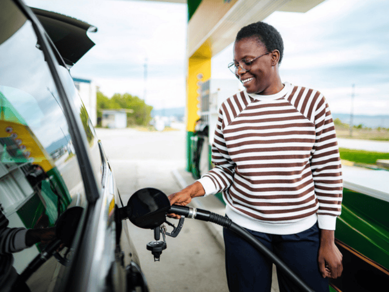 A young adult woman refueling her car at a petrol station