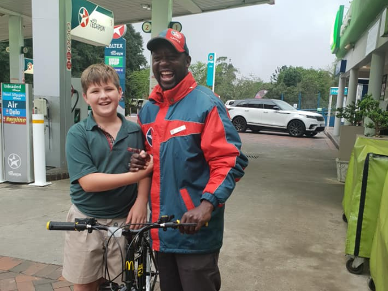 A young boy stands with a Caltex petrol attendant gifting him a bicycle