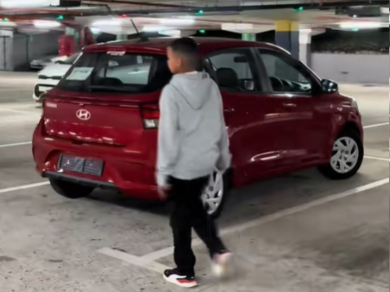 A young boy walking toward a new car parked inside carpark