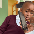 A young boy wearing a school uniform looks at the phone with is mother