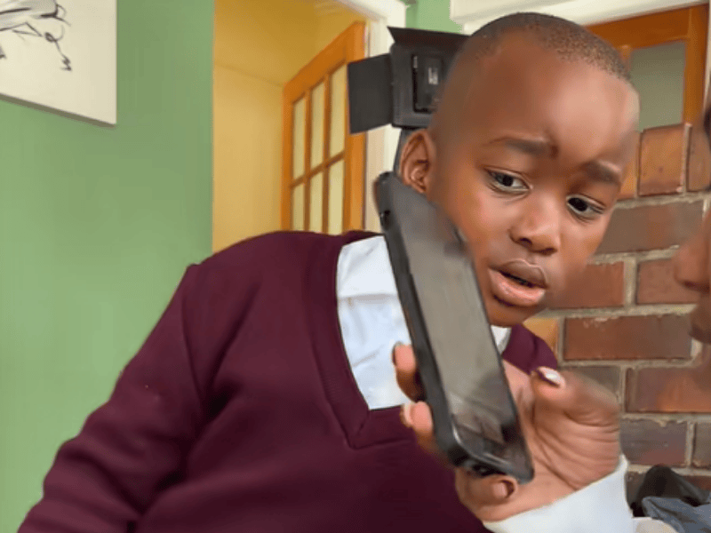 A young boy wearing a school uniform looks at the phone with is mother