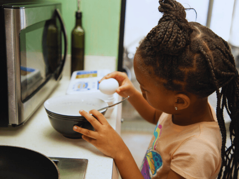 A young girl cracks an egg into a bowl