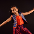 A young girl dressed in Indian attire holds her arms out as if in a dance move