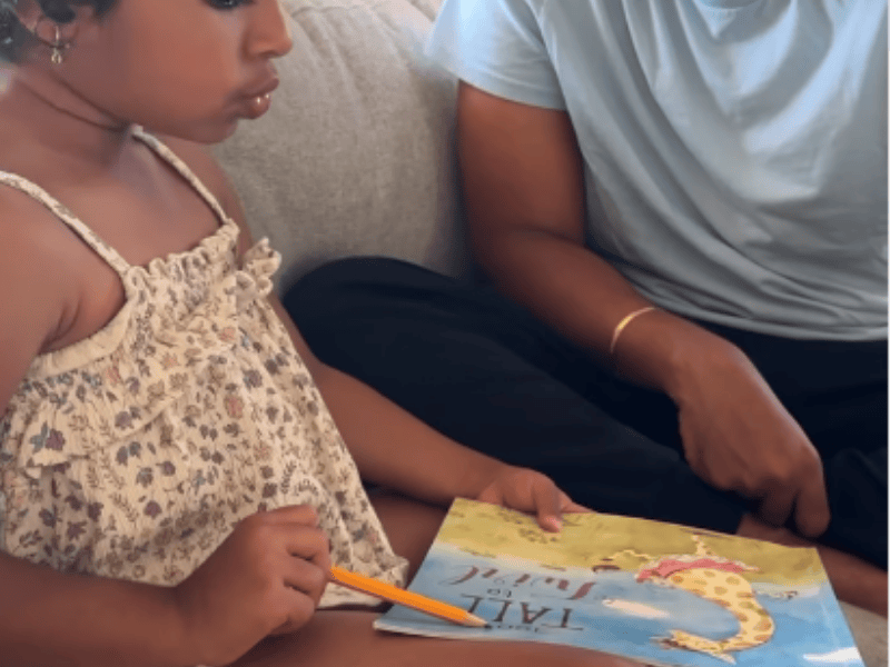 A young girl reading with her father on the couch