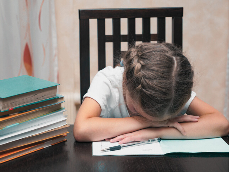 A young girl sleeping on her books while doing homework