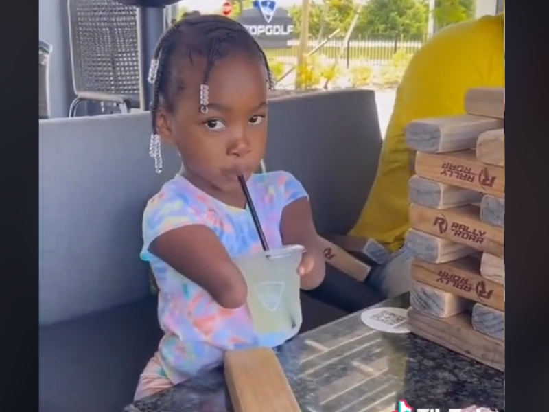 A young girl with braids drinks a juice