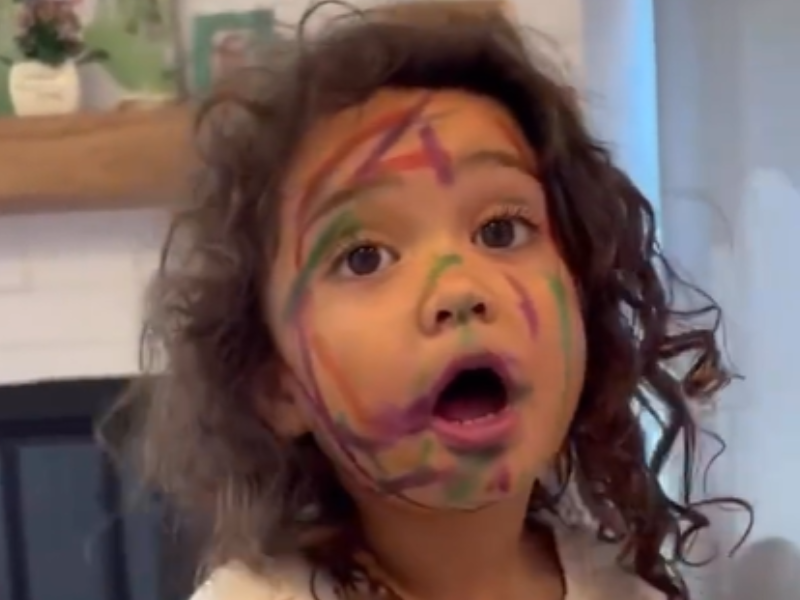 A young girl with curly hair with coloured marker drawings on her face